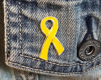 May include: A yellow ribbon pin on a denim jacket. The pin is a symbol of support for various causes.