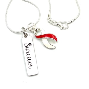 Può includere: Collana d'argento con un ciondolo a forma di nastro rosso e un'etichetta che dice "Survivor".