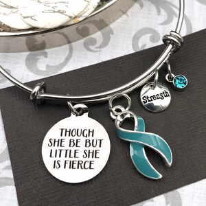 May include: A silver charm bracelet with a teal ribbon charm, a charm that says "Strength", and a charm that says "Though she be but little she is fierce".