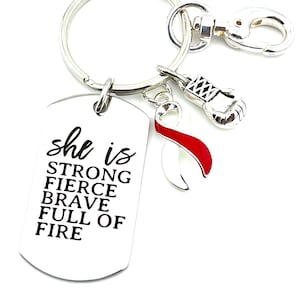 Può includere: Portachiavi d'argento con un'etichetta d'argento su cui è scritto "she is strong fierce brave full of fire". Il portachiavi ha anche un ciondolo a nastro rosso e un ciondolo a guanto da boxe argentato.