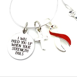 Può includere: Collana d'argento con tre ciondoli: un ciondolo rotondo con il testo "Ti sosterrò quando la tua forza fallirà", un ciondolo a croce e un ciondolo a nastro rosso e bianco.