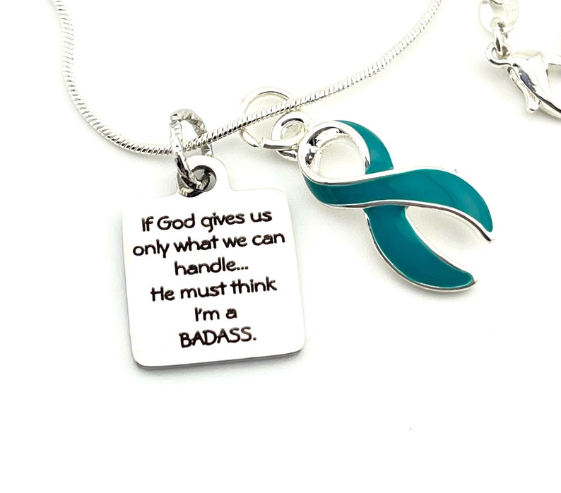 May include: Silver necklace with a teal ribbon charm and a square pendant with the text "If God gives us only what we can handle... He must think I'm a BADASS."
