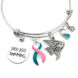 May include: A silver charm bracelet with a teal and pink ribbon charm, a fish charm, and a charm with the text "Just Keep Swimming".