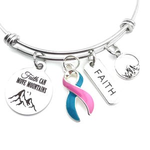 May include: Silver charm bracelet with multiple charms, including a teal and pink ribbon, a round charm with a mountain range and the text "Faith Can Move Mountains", and a rectangular charm with the word "FAITH".