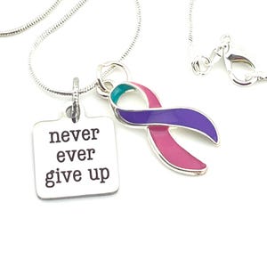 Puede incluir: Collar de plata con un dije cuadrado que dice "never ever give up" y un dije de cinta morado, rosa y turquesa.