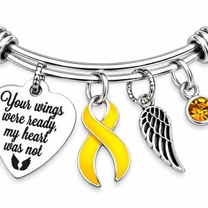 May include: A silver-tone bangle bracelet featuring four charms: a heart-shaped pendant engraved with the text "Your wings were ready, my heart was not" and a small wing icon, a yellow awareness ribbon, a detailed angel wing, and a yellow crystal.