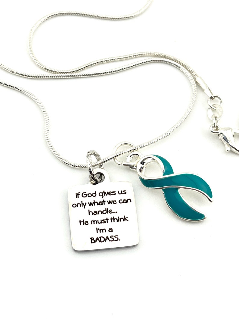 May include: Silver necklace with a teal ribbon charm and a silver pendant with the text "If God gives us only what we can handle... He must think I'm a BADASS."