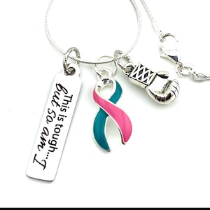 May include: Silver necklace with a charm that reads "This is tough... but so am I."  The necklace also features a teal and pink ribbon charm and a silver boxing glove charm.