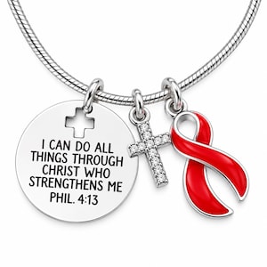 May include: A silver-toned snake chain necklace featuring three charms: a round disc engraved with the text I CAN DO ALL THINGS THROUGH CHRIST WHO STRENGTHENS ME PHIL. 4:13, a cross pendant encrusted with clear crystals, and a bright red awareness ribbon.