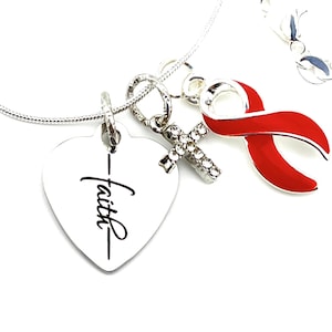 Può includere: Collana d'argento con un ciondolo a forma di cuore che dice "Fede" e un ciondolo a nastro rosso. La collana ha anche un piccolo ciondolo a croce con pietre.