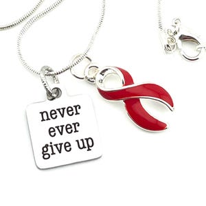 Può includere: Collana d'argento con un ciondolo a forma di nastro rosso e un ciondolo quadrato con le parole "never ever give up" incise.