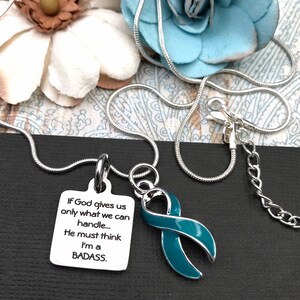 May include: A silver chain necklace with a teal ribbon charm and a silver charm with the text "If God gives us only what we can handle... He must think I'm a BADASS."