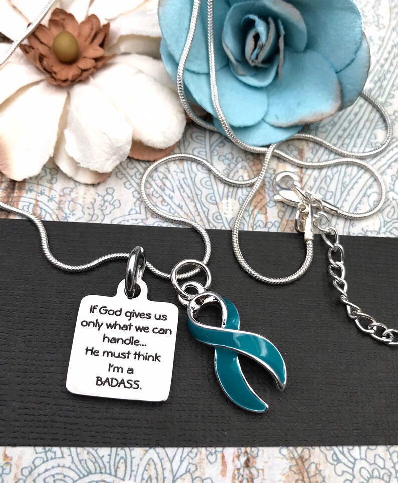 May include: A silver chain necklace with a teal ribbon charm and a silver charm with the text "If God gives us only what we can handle... He must think I'm a BADASS."