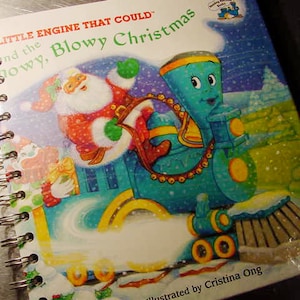 May include: A blue train engine with a snow plow, pulling a red and white train car with a Santa Claus figure. The book cover is titled "The Little Engine That Could and the Snowy, Blowy Christmas".