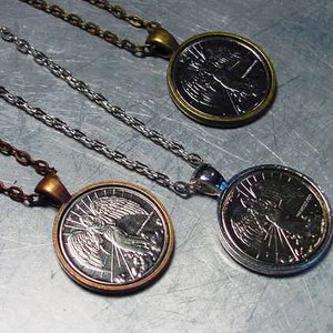 May include: Three silver necklaces with round pendants featuring an angel design. The pendants have a silver finish and are attached to silver chains.