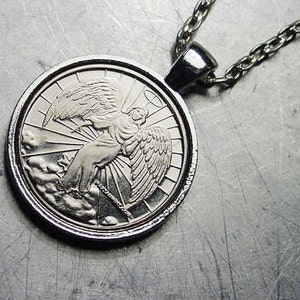 May include: Silver pendant necklace featuring a detailed image of an angel with wings spread, surrounded by a halo and rays of light. The pendant is attached to a silver chain.