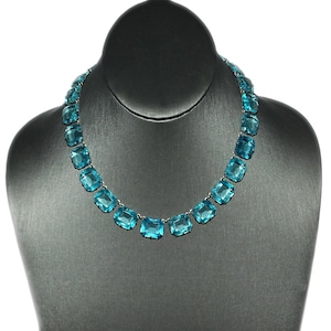 May include: A turquoise blue gemstone necklace with a silver chain. The necklace is made up of large, square-shaped gemstones.