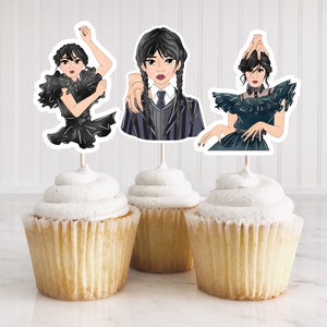 Pu&ograve; includere: Tre cupcakes sormontati da decorazioni a tema personaggio. Le decorazioni presentano illustrazioni di un personaggio in varie pose, vestito con abiti neri e blu scuro. I cupcakes hanno una glassa bianca e sono su una superficie bianca.