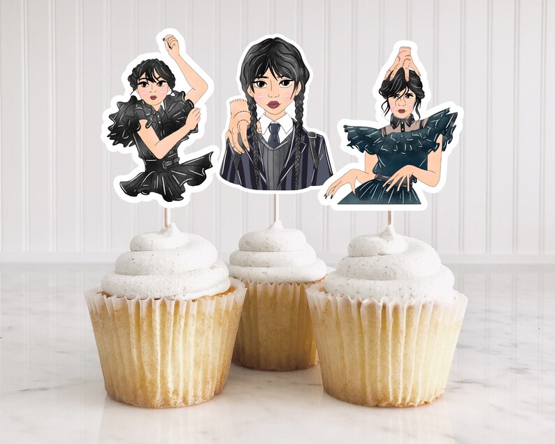 Pu&ograve; includere: Tre cupcakes sormontati da decorazioni a tema personaggio. Le decorazioni presentano illustrazioni di un personaggio in varie pose, vestito con abiti neri e blu scuro. I cupcakes hanno una glassa bianca e sono su una superficie bianca.