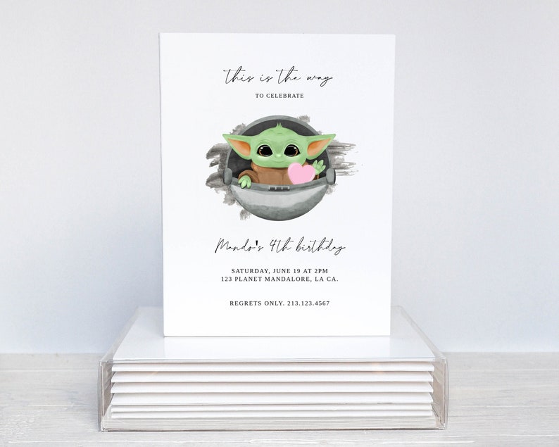 May include: A white invitation card with a green cartoon character holding a pink heart. The text on the card reads "this is the way to celebrate Mando's 4th birthday. Saturday, June 19 at 2PM 123 Planet Mandalore, LA CA. Regrets only. 213.123.4567"