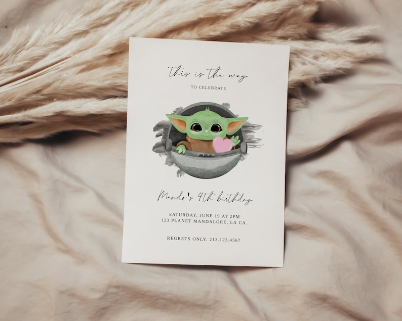 May include: A birthday invitation featuring a cartoon illustration of a green character from the Star Wars franchise, holding a pink heart. The text reads "This is the way to celebrate Mando's 4th birthday. Saturday, June 19 at 2PM, 123 Planet Mandalore, LA CA. Regrets only. 213.123.4567"