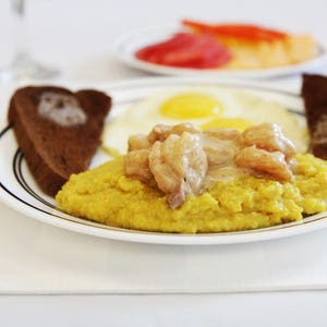 May include: A plate of yellow grits with shrimp and a creamy sauce, served with two slices of toasted bread and two fried eggs.