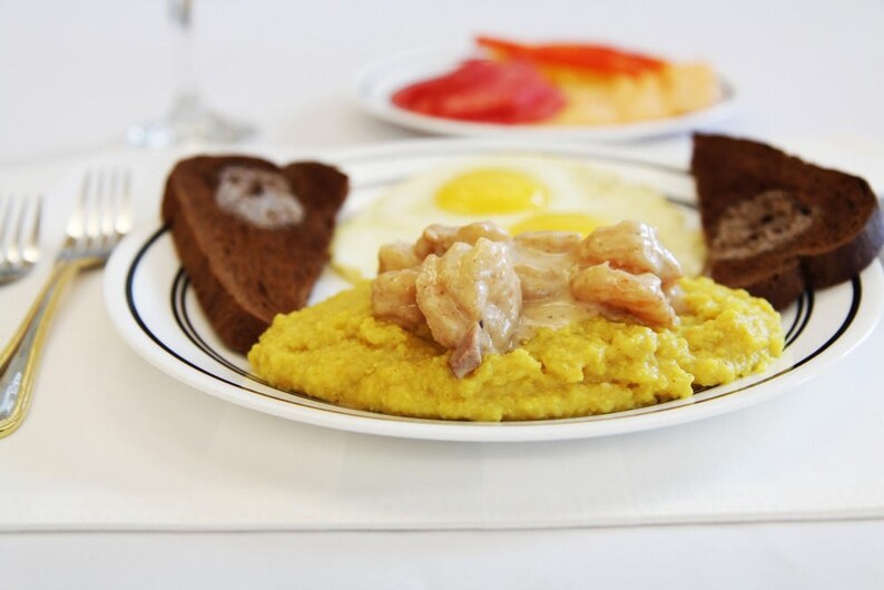 May include: A plate of yellow grits with shrimp and a creamy sauce, served with two slices of toasted bread and two fried eggs.