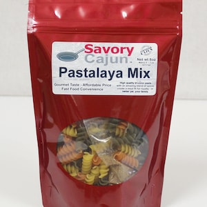 May include: Red resealable pouch with a clear window showing tri-color pasta. The pouch has a label that reads "Savory Cajun Pastalaya Mix" with the text "Gourmet Taste - Affordable Price Fast Food Convenience" and "High quality tri-color pasta with an amazing blend of spices create a meal fit for royalty - or better yet, your family."