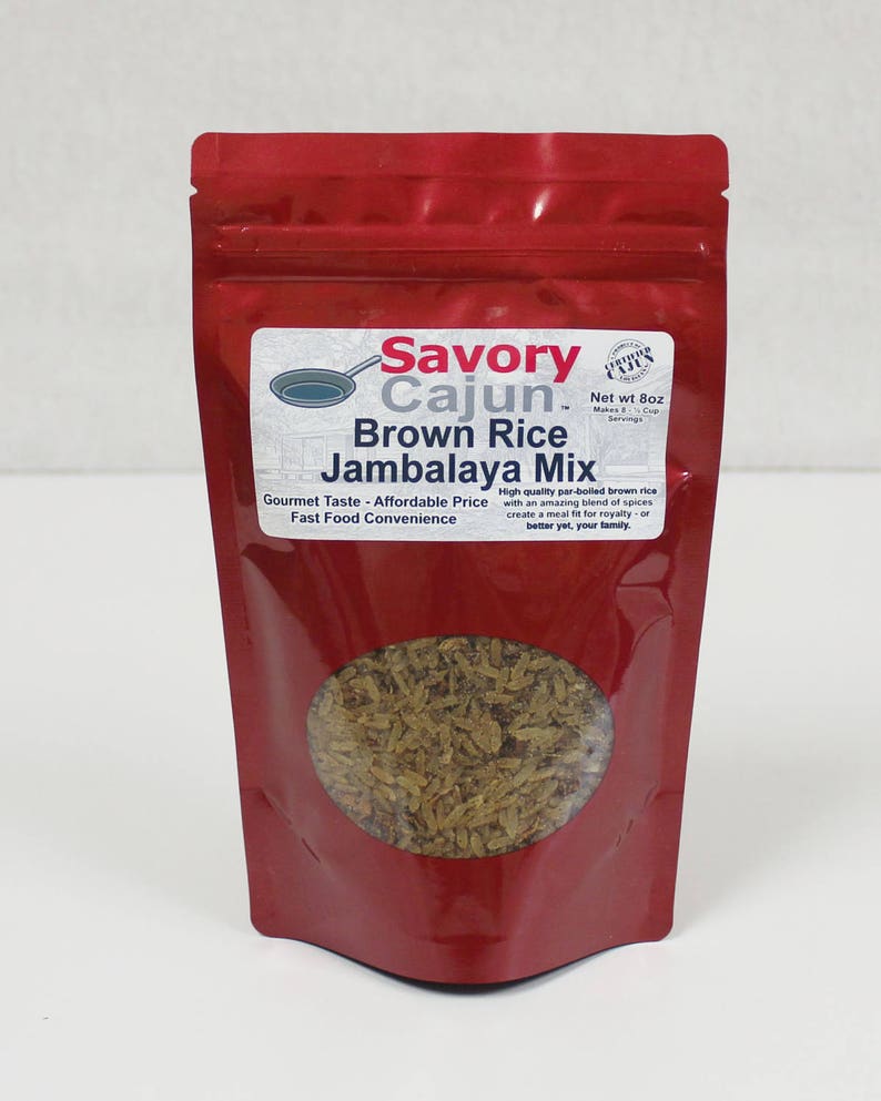 May include: A red pouch of Savory Cajun Brown Rice Jambalaya Mix. The package has a clear window showing the brown rice mix. Text on the label reads "Gourmet Taste - Affordable Price" and "Fast Food Convenience."