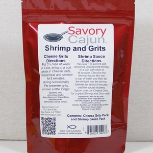 May include: A red resealable pouch with a white label that reads "Savory Cajun Shrimp and Grits". The label includes instructions for preparing cheese grits and shrimp sauce. The pouch contains a pack of cheese grits and a pack of shrimp sauce mix.