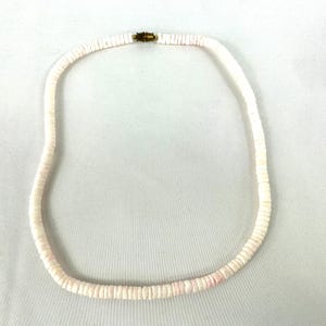May include: A white shell necklace with a gold clasp. The necklace is made of small, round shells that are strung together.