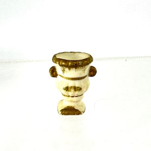 May include: A small white ceramic planter with gold accents. The planter has a round body and two handles.