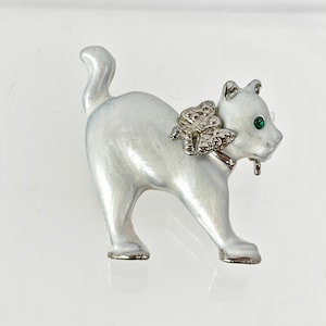 May include: A white ceramic cat brooch with a silver butterfly on its neck and green rhinestone eyes.