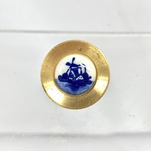 May include: A brass button with a blue and white porcelain inlay depicting a windmill. The porcelain is surrounded by a gold rim.