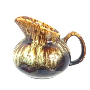 May include: A brown and white glazed ceramic pitcher with a brown handle. The pitcher has a mottled glaze with brown and white streaks.