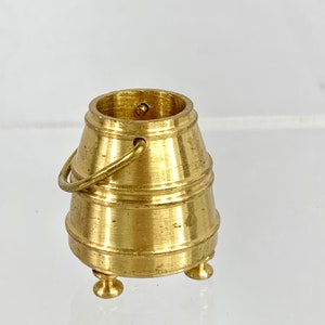May include: A small, gold-colored metal bucket with a handle and three legs. The bucket is about 2 inches tall.
