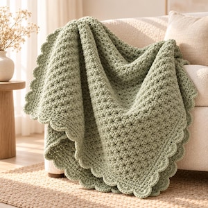 May include: A sage green crochet blanket featuring a textured starburst stitch pattern throughout the body and a decorative scalloped edge border. The soft yarn construction creates a thick, folded drape over the side of a couch.