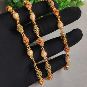 May include: A gold-tone chain necklace featuring a series of spherical beads with a lattice-like metal overlay. The beads are accented with alternating red, green, and white enamel or stone inserts, connected by small gold-tone metal links.