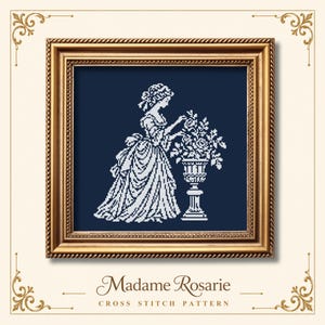 Pode incluir: Um padrão de ponto cruz intitulado Madame Rosarie apresentando a silhueta branca de uma pessoa com vestido de época ao lado de uma urna floral num fundo azul escuro, numa moldura dourada decorativa com cantos ornamentados.