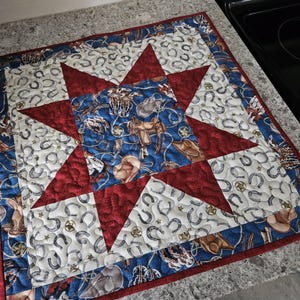 May include: A red, white and blue quilted table runner with a star design. The fabric features a pattern of horseshoes, cowboy hats and other western motifs.