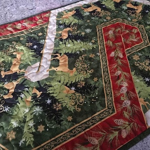 Peut inclure: Chemin de table de Noël matelassé au design festif. Le chemin de table présente un fond vert avec des cerfs, des arbres et des flocons de neige. Des bordures rouges avec des motifs de pommes de pin et de feuilles ajoutent une touche saisonnière. Environ 152 cm de long.
