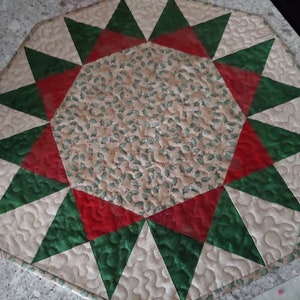 May include: A quilted table runner with a starburst design in red, green, and cream. The center of the runner features a holly leaf pattern.