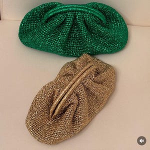 May include: Two metallic clutch purses. One is a vibrant green, the other a shimmering gold. Both have a gathered design and a rounded shape. The purses are made of a woven material, giving them a textured appearance. They are ideal for evening wear.