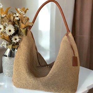 May include: A large, tan crocheted tote bag with brown leather handles. The bag is made of a thick, woven material and has a slouchy, casual look.