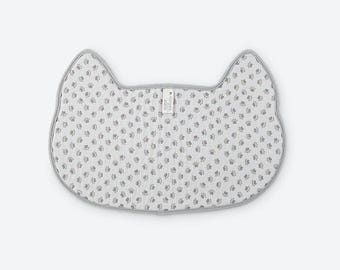 May include: A cat-shaped mat featuring a white base with a repeating pattern of small gray paw prints. The mat has a gray fabric border and a small white rectangular tag at the top center with the text Norwex printed in black.