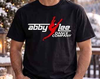 May include: A black short-sleeved t-shirt featuring a white graphic logo that reads "abby lee" with a red silhouette of a dancer in the centre and the text "DANCE COMPANY" printed in white underneath the dancer figure.