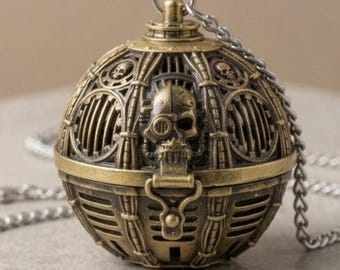 May include: A spherical brass-toned metal pendant featuring a central skull motif with a mechanical eye piece, surrounded by cage-like vertical bars and smaller skull accents. The object includes a top loop attached to a silver-toned metal chain.