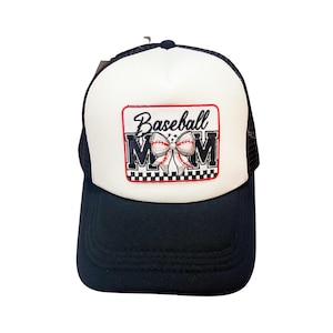 Puede incluir: Gorra de béisbol negra y blanca con parte trasera de malla y visera curva. El panel frontal es blanco con un parche rectangular con las palabras "Baseball MOM" y un gráfico de béisbol.