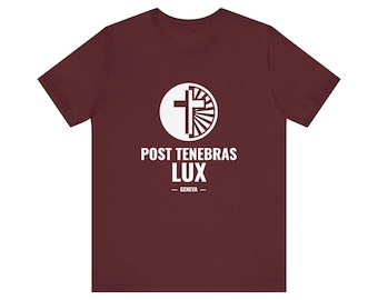 Op de afbeelding: Een bordeauxrood t-shirt met korte mouwen en een witte cirkelvormige afbeelding met een kruis en een zonnestraalontwerp. Onder de afbeelding staat de tekst POST TENEBRAS LUX en GENEVA in witte hoofdletters op de borst.