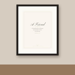 May include: A framed wall art print featuring the text A Friend, followed by the quote A friend loveth at all times, and a brother is born for adversity, and the reference Proverbs 17:17, centered on a cream background with a black frame.
